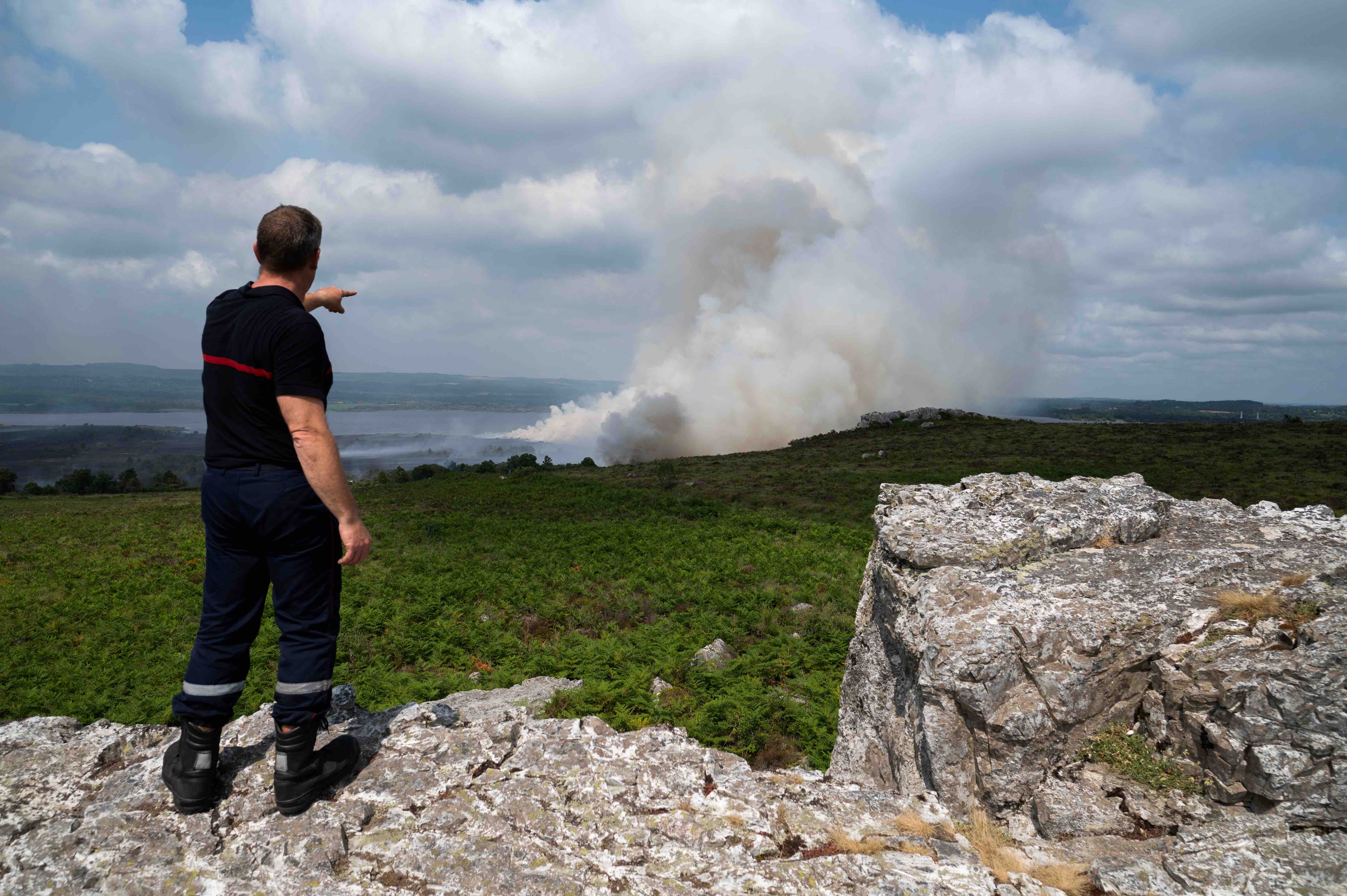Un pompier montre l'incendie qui fait rage sur les Monts d'Arrée, le 19 juillet 2022 - Loic Venance / AFP